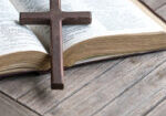 Wooden cross on top of an open bible and wood table. Copy space.