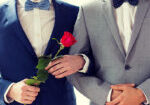 people, homosexuality, same-sex marriage and love concept - close up of happy male gay couple with red rose flower holding hands on wedding
